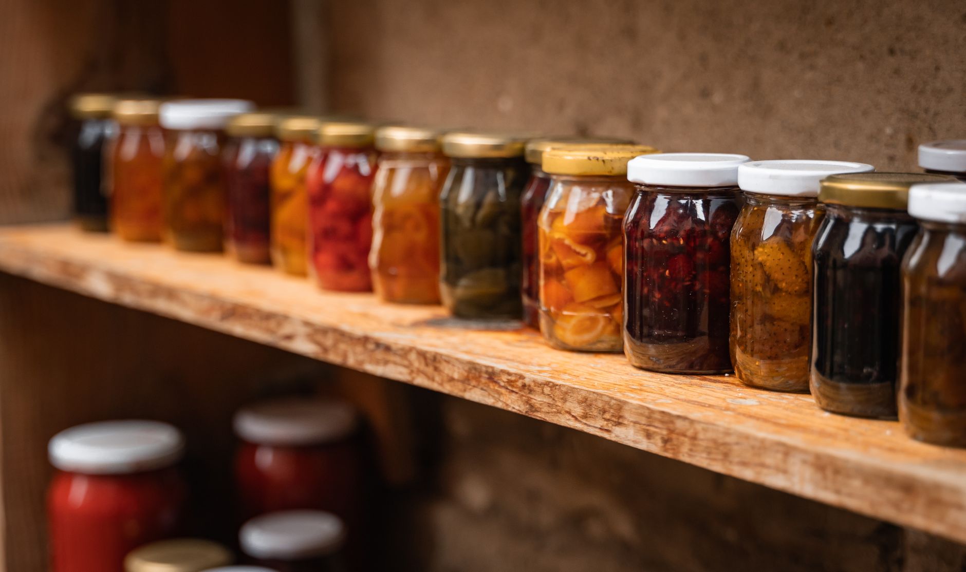 Rows of home-canned jars filled with preserved vegetables on a wooden shelf